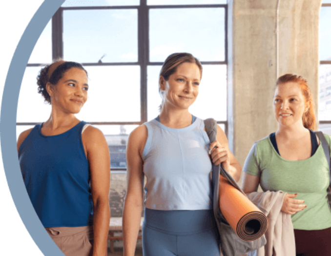 Tres mujeres conversando, una de ellas sosteniendo una colchoneta de ejercicio